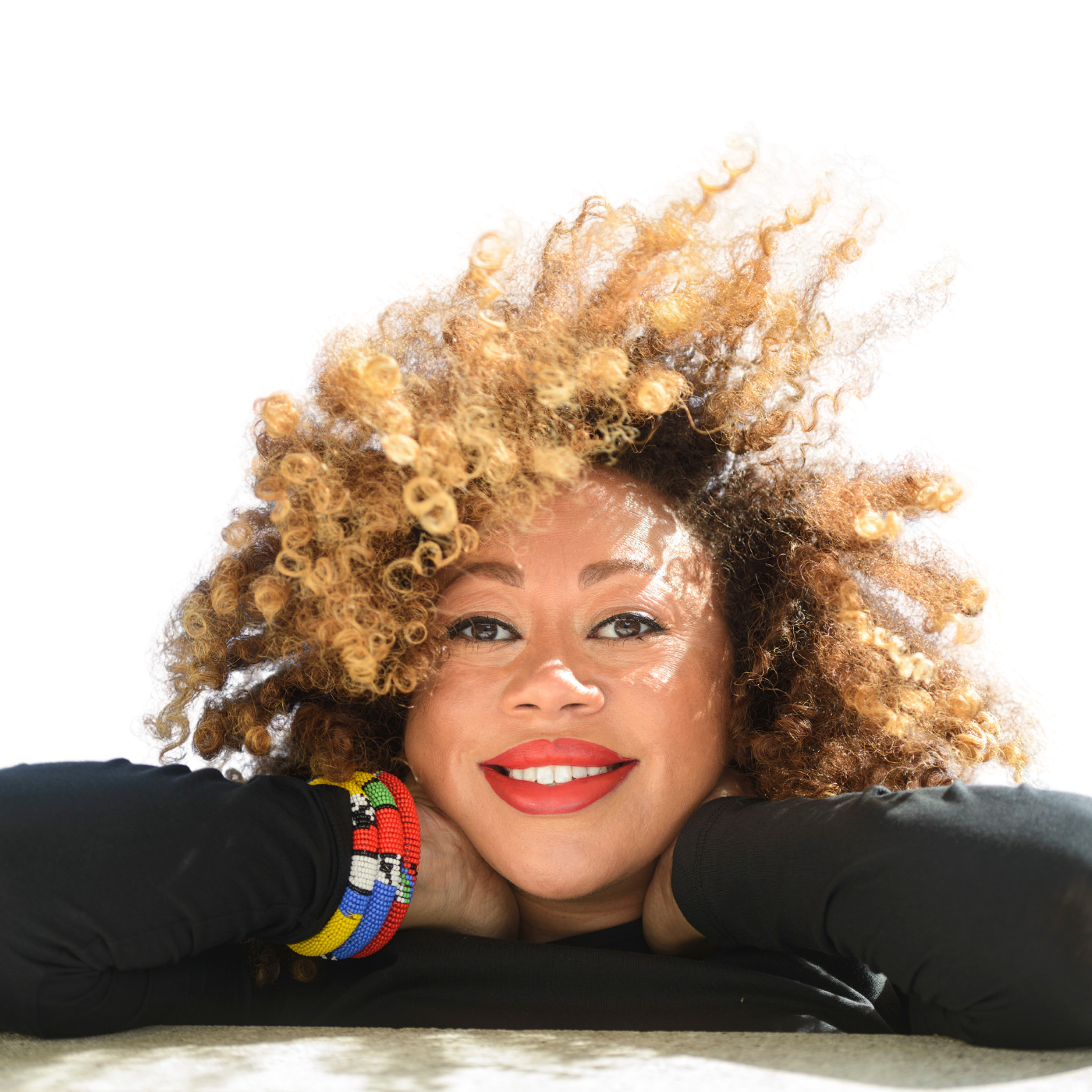 Picture of Ithalia with voluminous curly hair wearing black clothing and colorful beaded bracelets against white background.
